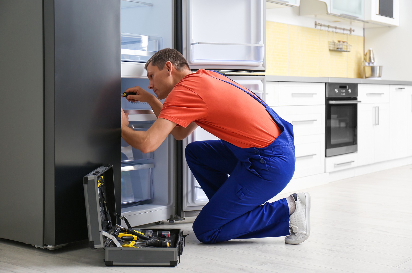 Technician inspecting an open residential refrigerator with a screwdriver and toolkit