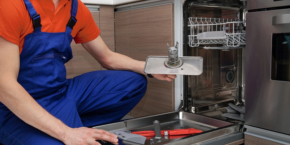 Technician holding a dishwasher filter beside an open dishwasher