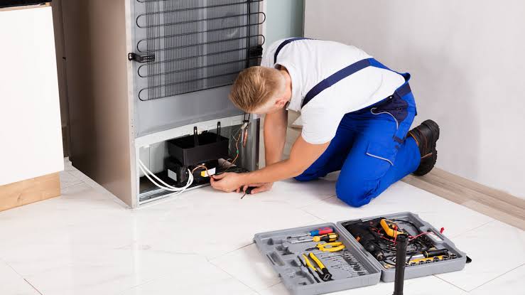 Technician checking components at the back of a refrigerator