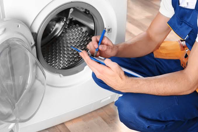 Technician recording diagnostic notes beside an open front-load washer